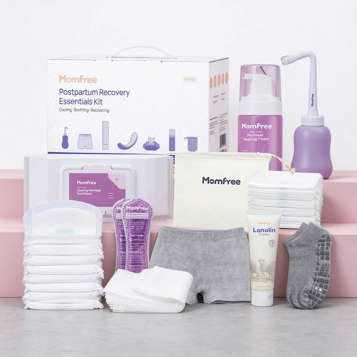 Momfree Ultra postpartum recovery kit with peri bottle, foam, cream, underwear, pads, socks, and bag arranged on a gray surface.