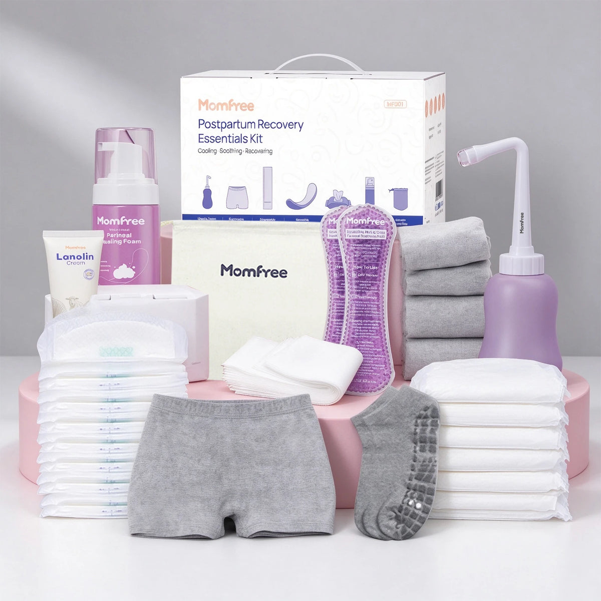Momfree Ultra postpartum recovery kit on pink display blocks with underwear, pads, socks, peri bottle, foam, cream, and storage bag.